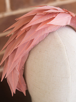 Close up of dusty pink headband. There are feathers on one side of the headband.