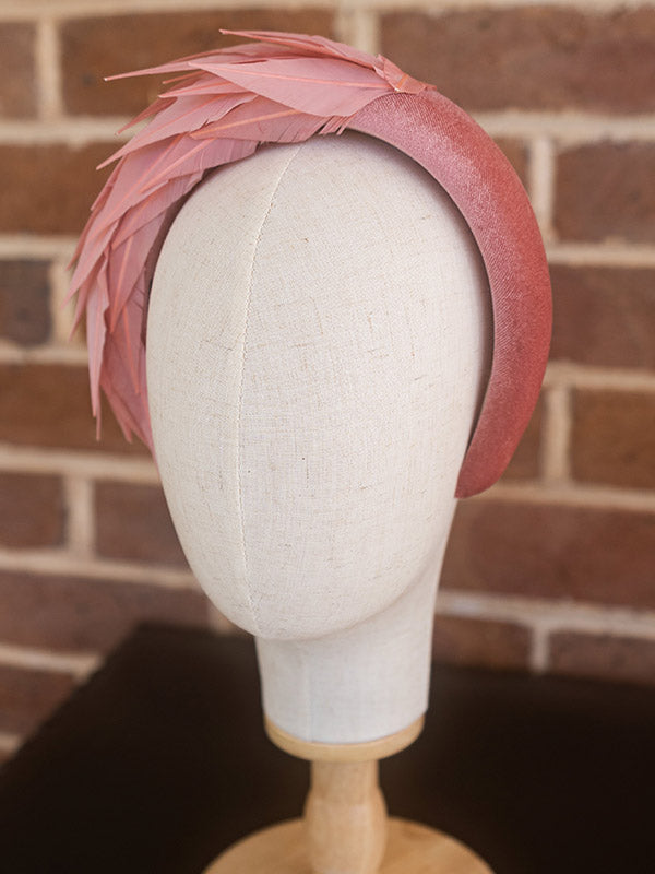 Side view of dusty pink headband. There are feathers on one side of the headband.