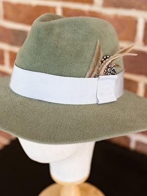 Close up of soft green felt fedora hat with beige coloured feathers.