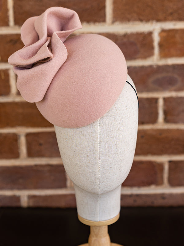 Front view of baby pink felt cocktail hat. The hat has a large felt bow on the top of it.