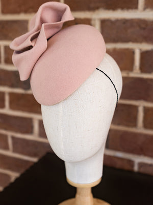 Side view of baby pink felt cocktail hat. The hat has a large felt bow on the top of it.