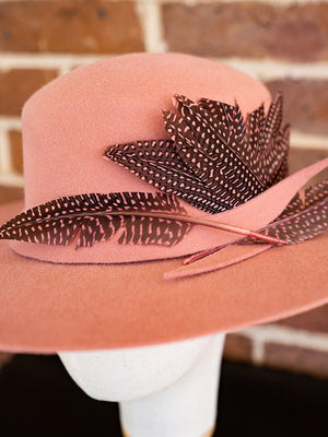 Close up of salmon pink felt hat trimmed with spotty pink dyed feathers.