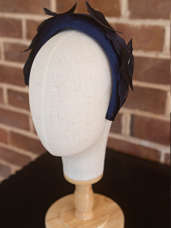 Side view of blue velvet headband. Black feathers sit slightly curved around the headband.