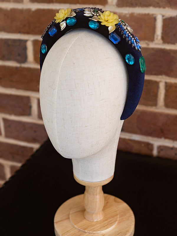 Side view of the blue velvet headband. Colourful beading and gemstone detailing is placed all around the headband.