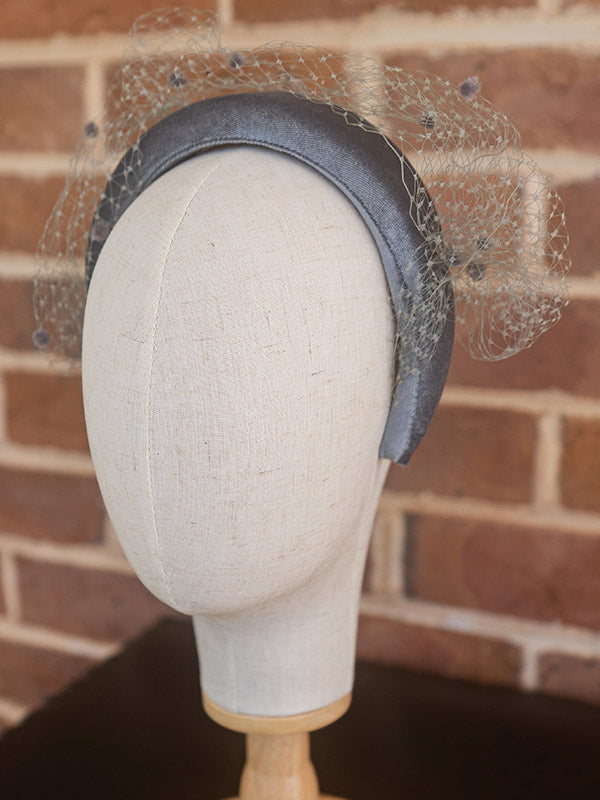 Side view of grey velvet headband. Grey spotted netting sits over the top of the headband.