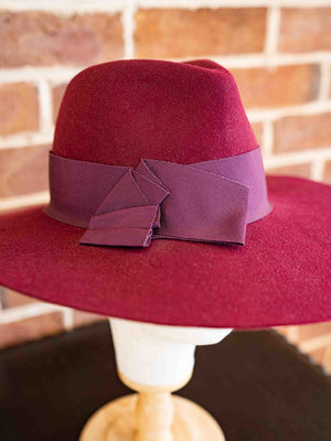 Close up mulberry wide brimmed fedora felt hat with dark red ribbon.