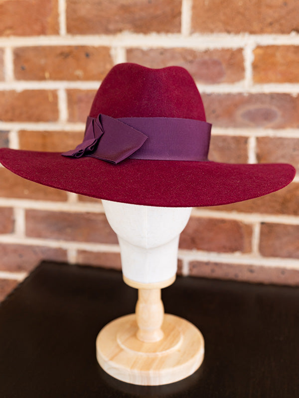 Side view mulberry wide brimmed fedora felt hat with dark red ribbon.