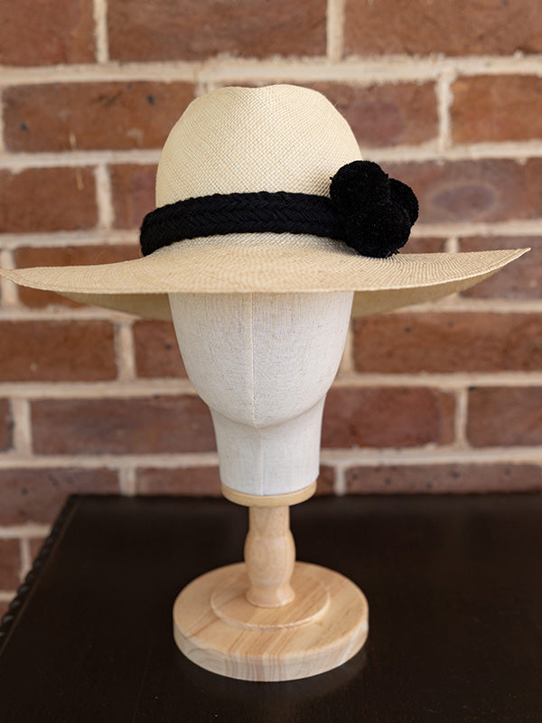 Front view of natural panama fedora hat with black pom pom trim.