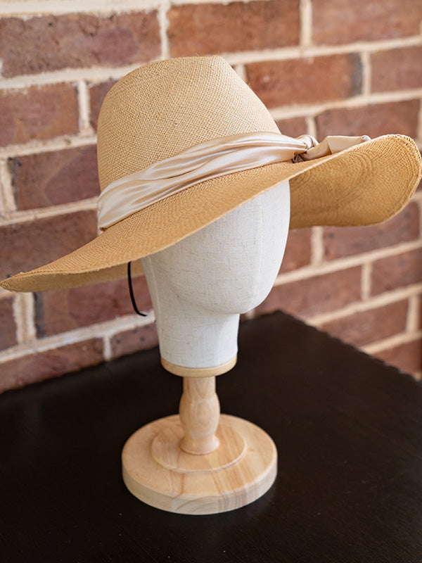 Side view of natural panama fedora hat. A light pink silk band sits around the hat.