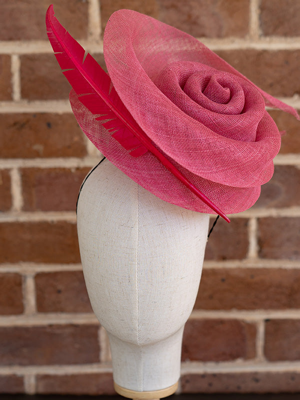 Front view of the sinamay cocktail hat with a beautiful pink swirl and single pink feather on one side.