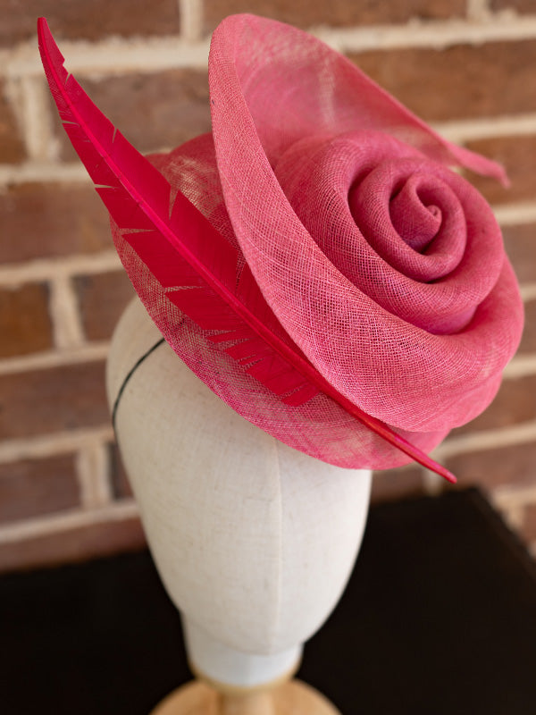 Side view of the sinamay cocktail hat with a beautiful pink swirl and single pink feather on one side.