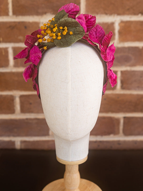 Front view of vintage inspired headpiece adorned with pink and green leaves and small yellow button shaped flowers.