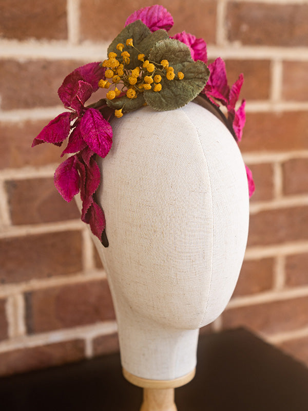 Side view of vintage inspired headpiece adorned with pink and green leaves and small yellow button shaped flowers.