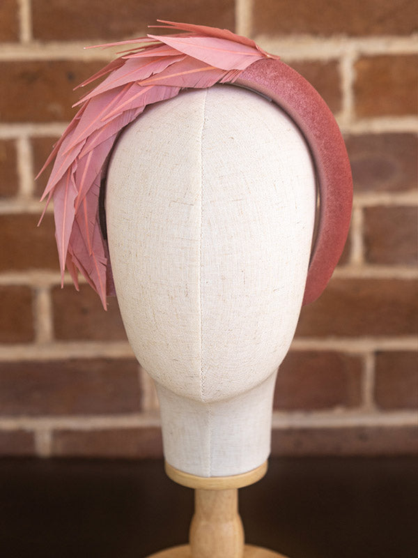 Front view of dusty pink headband. There are pink feathers on one side of the headband.