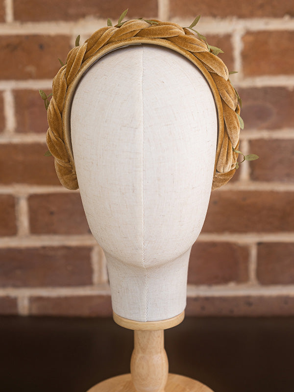 Front view of mustard coloured headband with small green leaves scattered on top.