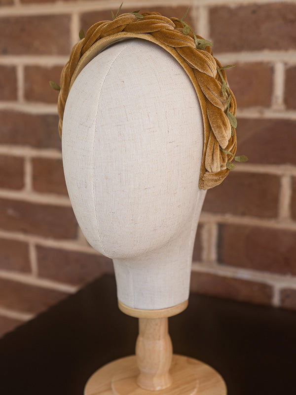 Side view of mustard coloured headband with small green leaves scattered on top.