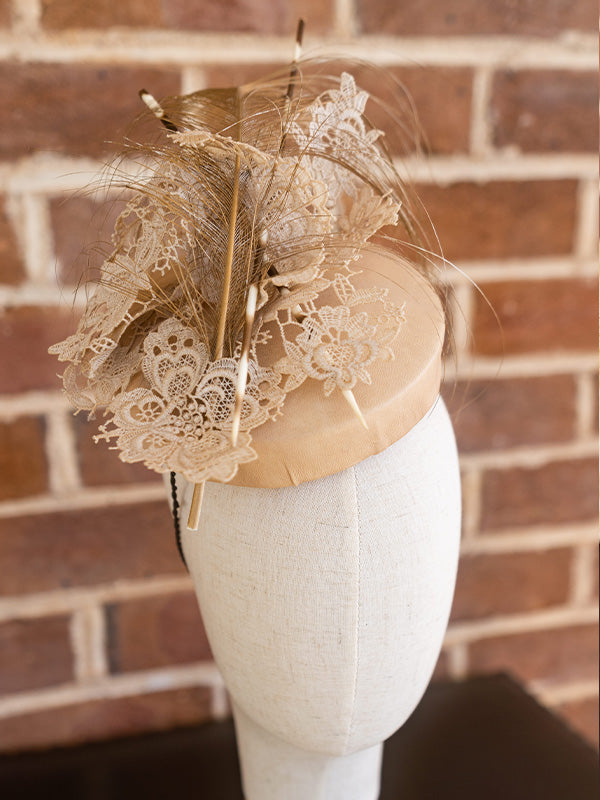 Front view of nude leather cocktail hat with nude lace, feather and net trimming.