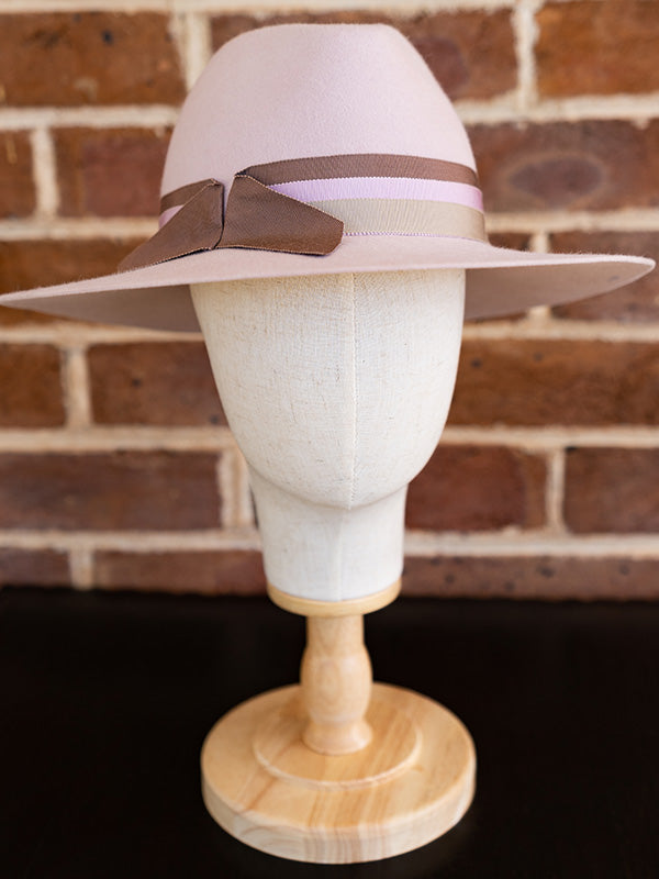 Front view of pink felt fedora hat with three ribbons wrapped around the hat.