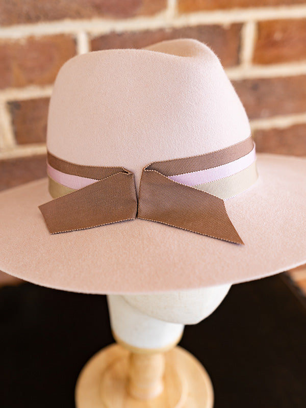 Close up of pink felt fedora hat with three ribbons wrapped around the hat.