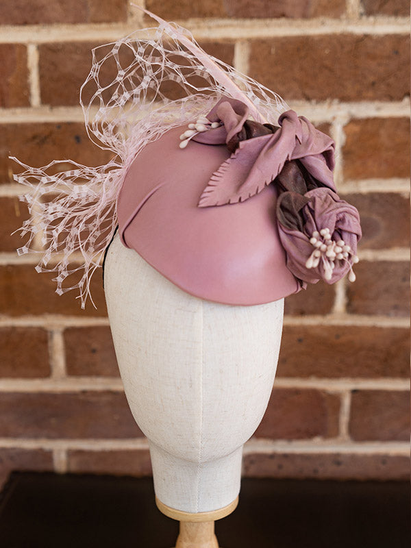 Front view of pink leather cocktail hat with flowers and pink netting.