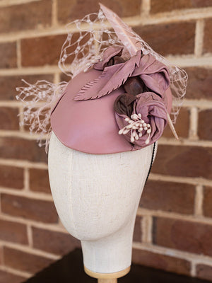 Side view of pink leather cocktail hat with flowers and pink netting.