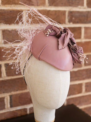 Side view of pink leather cocktail hat with netting and floral detail.